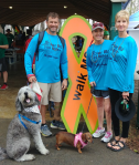 3 people with 2 dogs standing next to a ribbon for MS