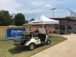 Golf cart next to softball field and dugout with Encore Sports Medicine Banner in the background during a bright spring day