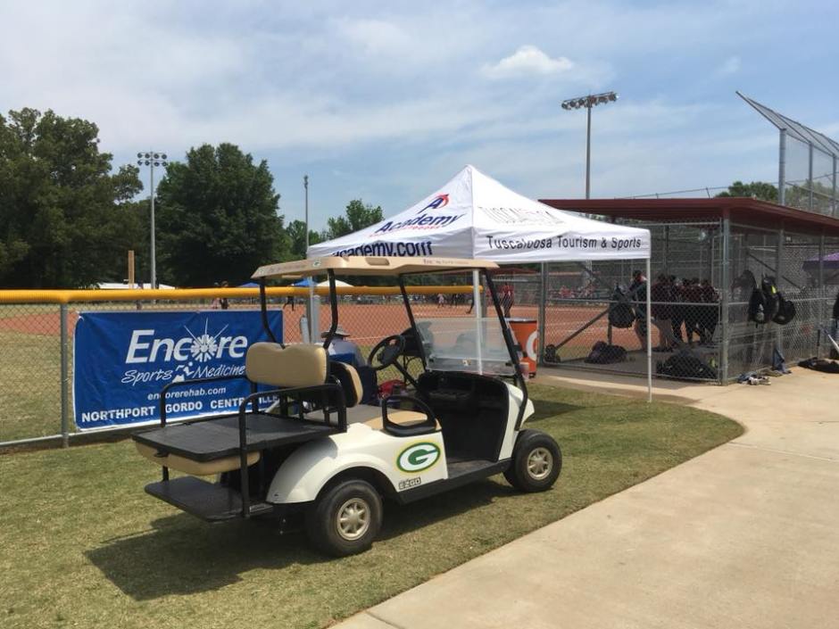 Golf cart next to softball field and dugout with Encore Sports Medicine Banner in the background during a bright spring day