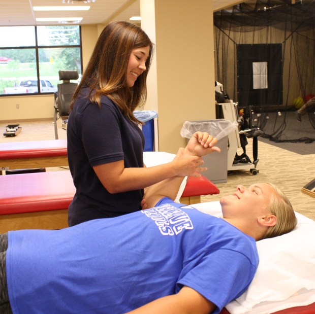 Female Physical Therapist performing shoulder exercises with young lady lying on rehab treatment table