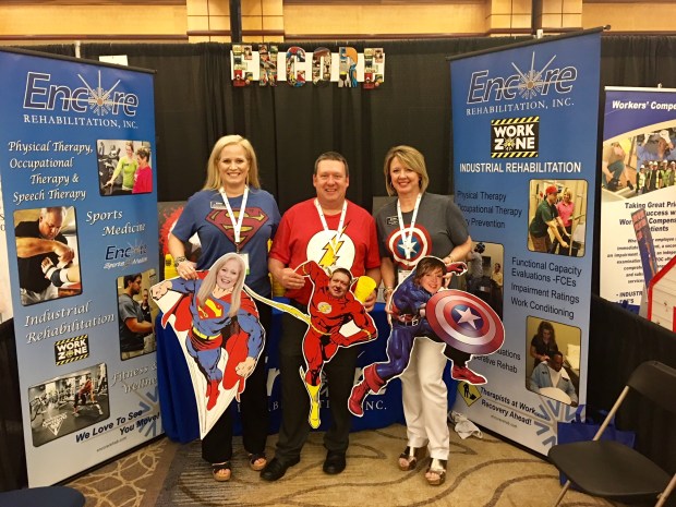 Encore Rehabilitation booth with employees with super heroes t-shirts depicting superman, the flash, and captain america.