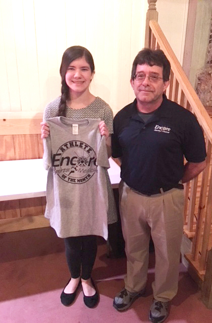 Young female athlete holding a gray Encore Sports Medicine athlete of the month t-shirt poses with Athletic Trainer Dewayne Fortenberry