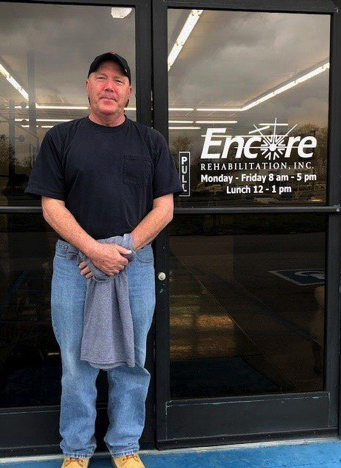man smiling, posing in front of the glass doors to Encore Rehabilitation-Russellville clinic