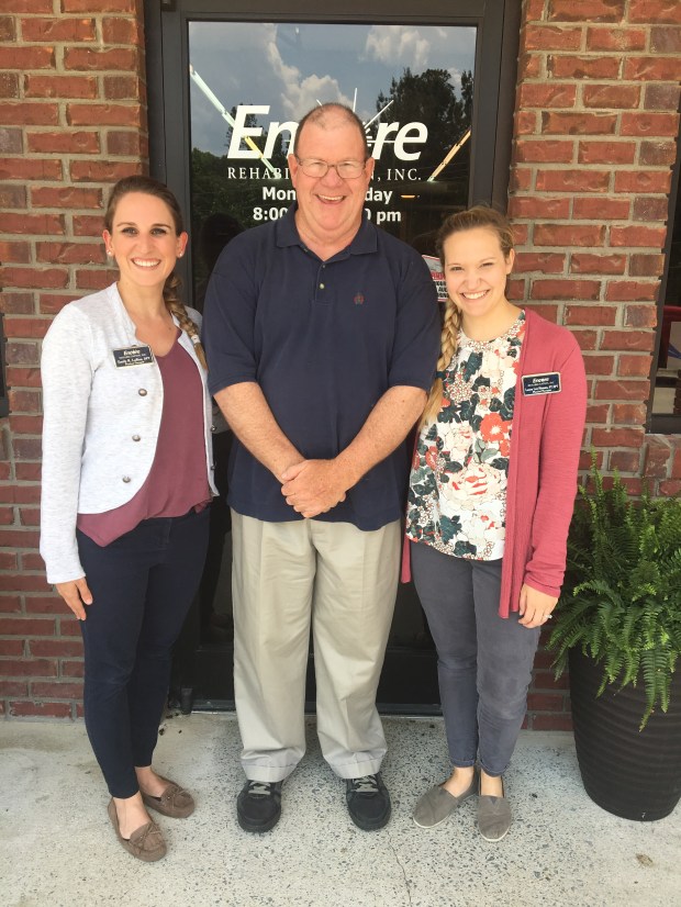 One man and two women posing and smiling in front of the door to the Encore Rehabilitation-Hayden Clinic.